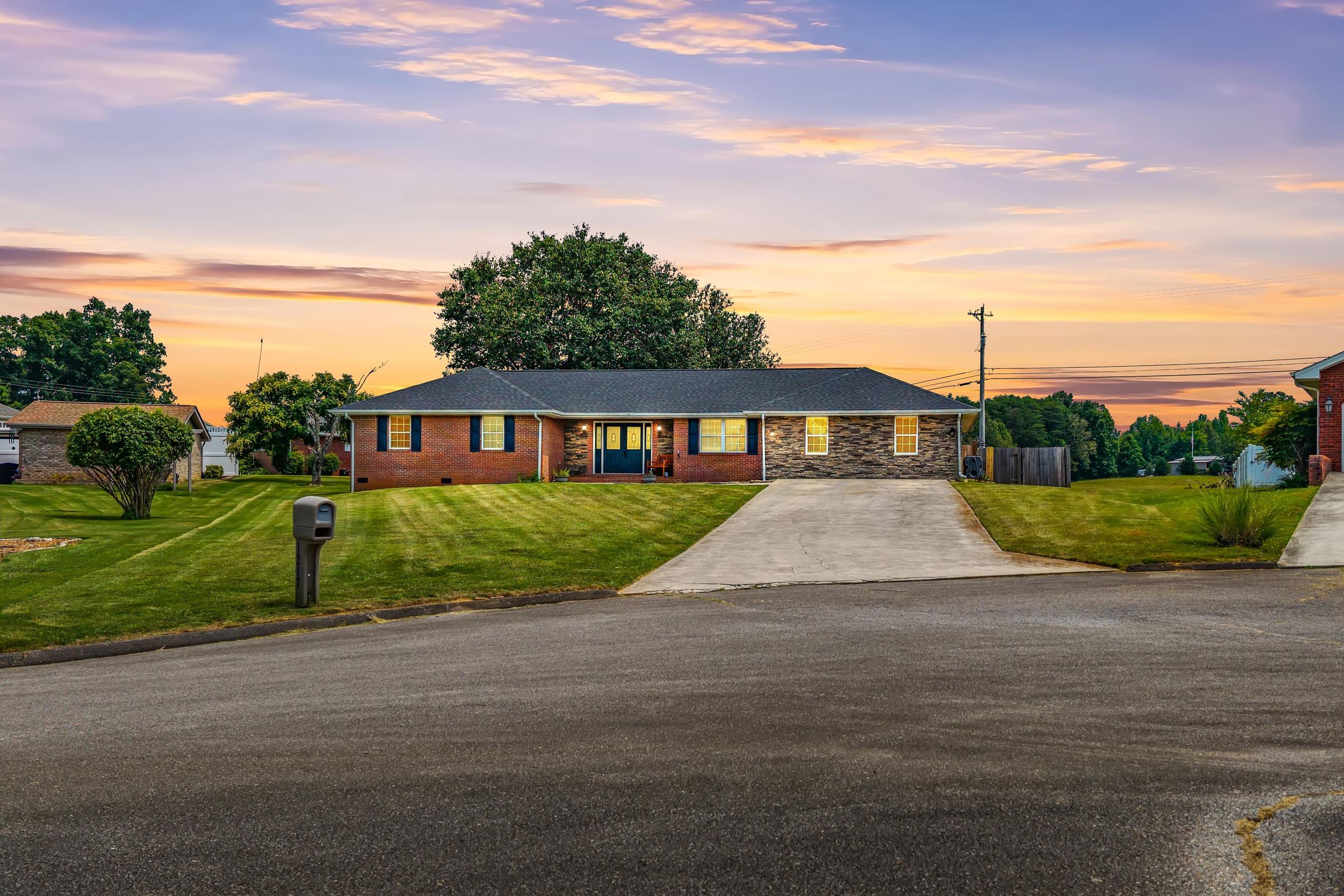 1217 Cedar Lane at sunset, a brick and stone ranch home with the lights on and a long driveway